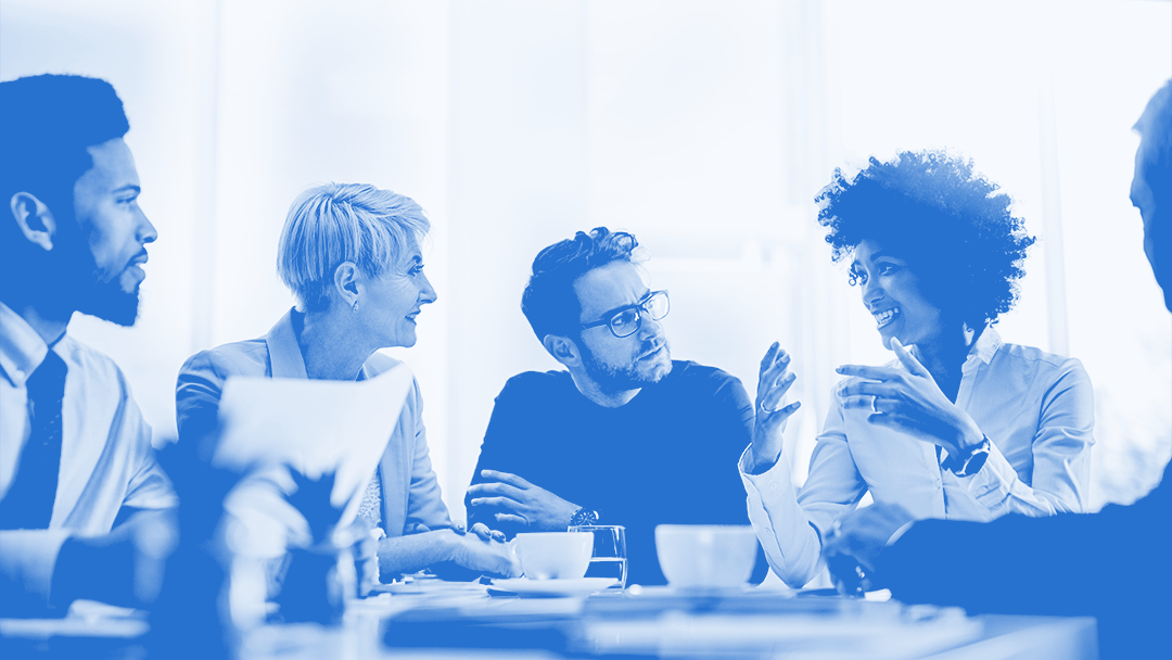 A blue-hued image of five gender-diverse team members sitting around a table